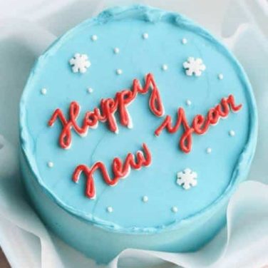A light blue New Year cake with "Happy New Year" in red icing and snowflake decorations.