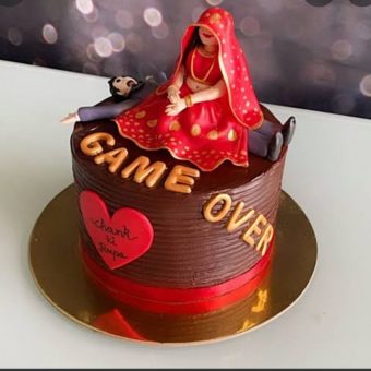 Wedding cake with bride and groom figurine on top. Text on cake reads "Game Over"