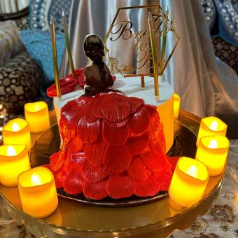 Bachelorette party cake with 'Bride to Be' topper and LED candles on a glass table.