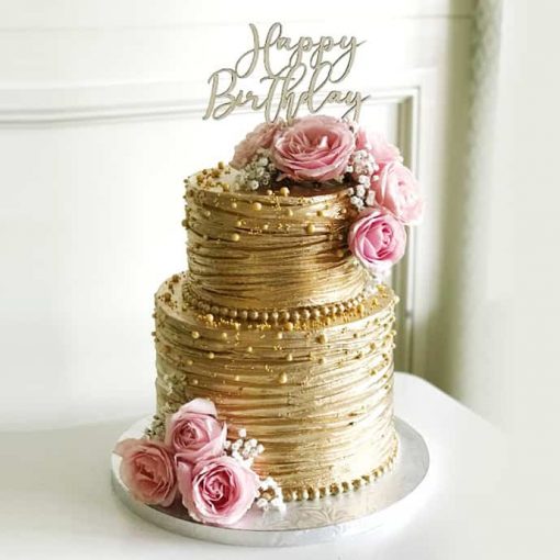 Two-tier golden birthday cake adorned with pink roses