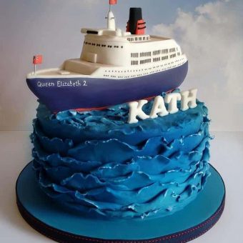 Ocean wave cruise ship cake with a Queen Elizabeth 2 ship model on top and name 'KATH' in fondant letters.