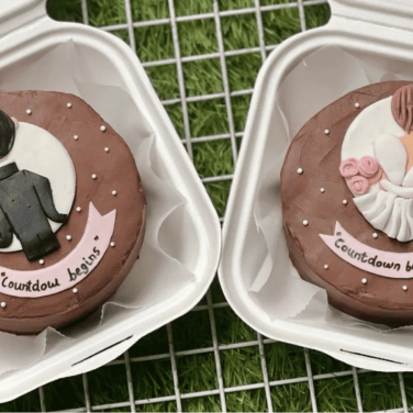 Two round cakes in white containers, one decorated with a groom's suit and ring, the other with a bride in a dress and roses, both with 'Countdown begins' written on them.