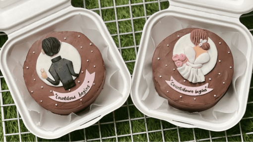 Two round cakes in white containers, one decorated with a groom's suit and ring, the other with a bride in a dress and roses, both with 'Countdown begins' written on them.