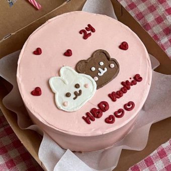 A pink cake with a smooth icing finish, topped with two cartoon animal faces, one white and one brown