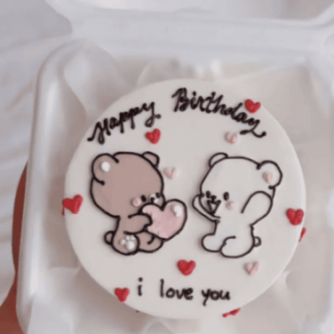 A round shape cake with two cute teddy couple and happy birthday written lots of hearts