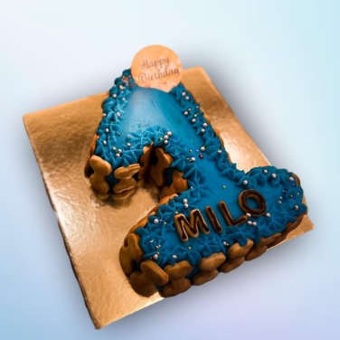 Blue number 1 dog birthday cake with name “Milo,” decorated with dog biscuits, frosting, and pearl