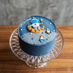 Dark blue cream cake with astronaut on moon and rocket ship flat art.