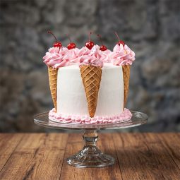 White cake decorated with pink frosting scoops in waffle cones topped with cherries.