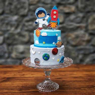 Two-tier blue space cake with cartoon astronaut and rocket toppers.